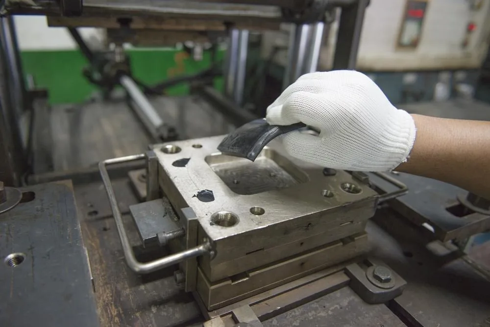 Technician removing a moulded rubber component from a steel mould in the workshop